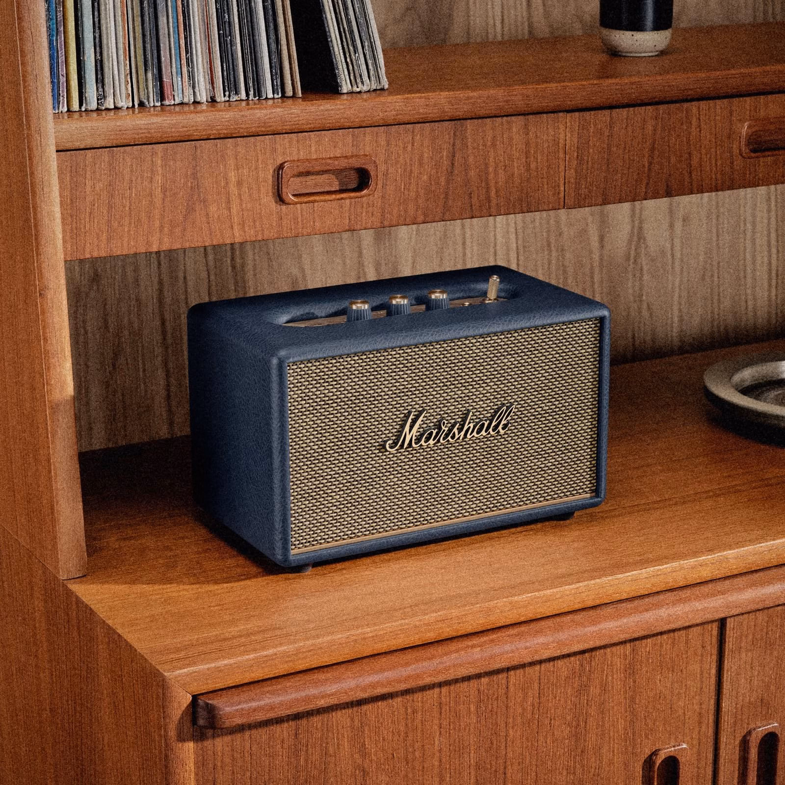 Акустическая колонка Marshall Acton III Midnight Blue на деревянной тумбе рядом с винилом.