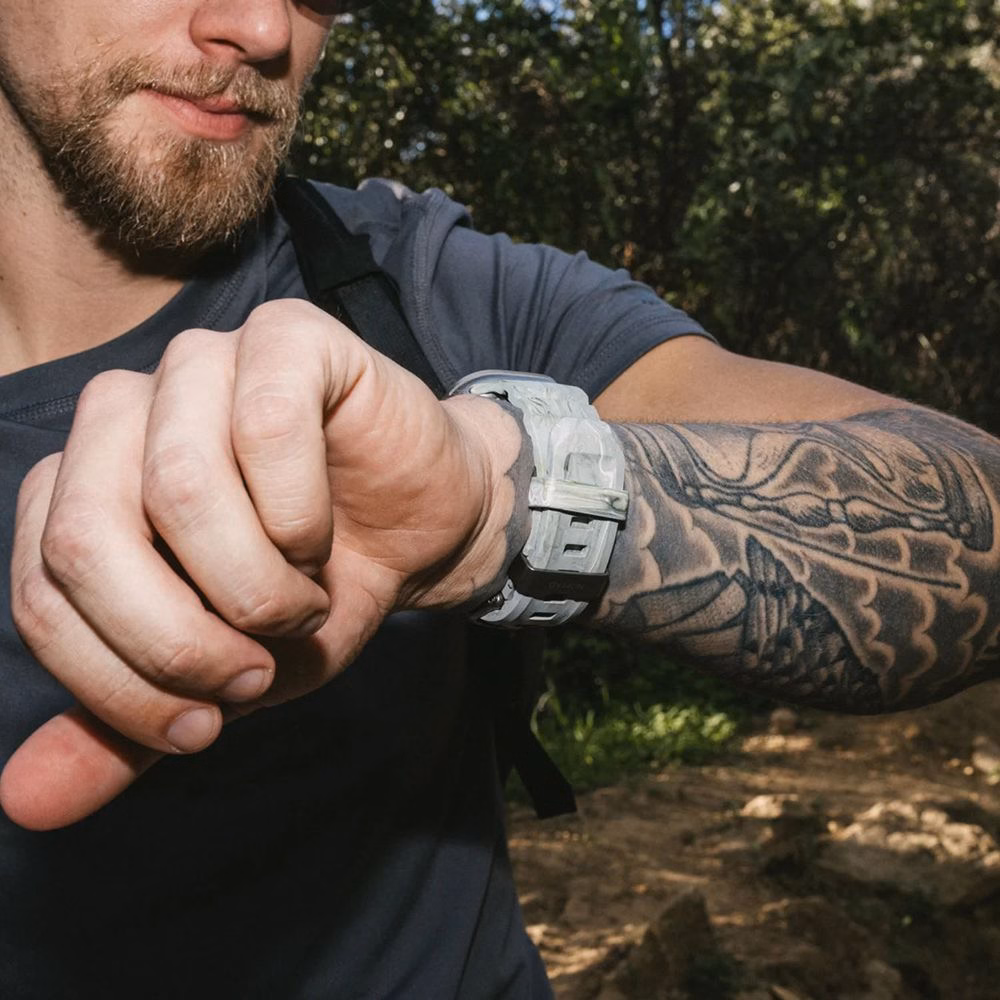 Пользователь проверяет маршрут на Apple Watch с ремешком Nomad Rocky Point Sierra Stone во время горного похода.