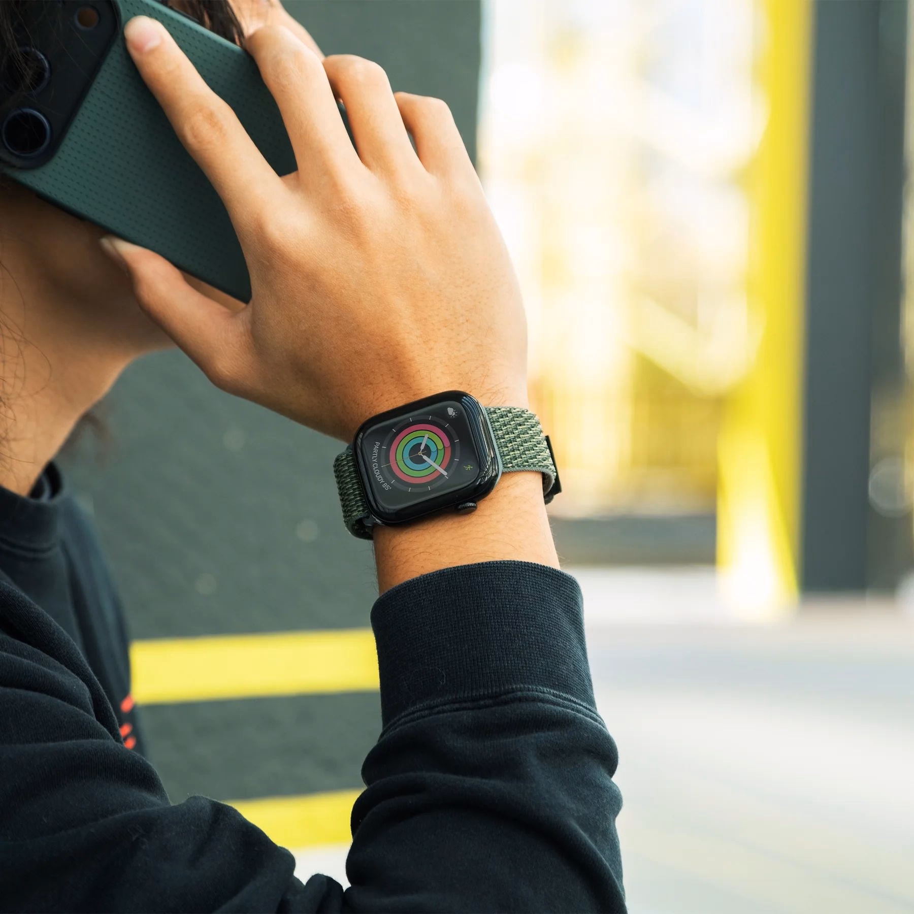 Ремешок Slate Green на мужской руке, держащей iPhone в фирменном чехле