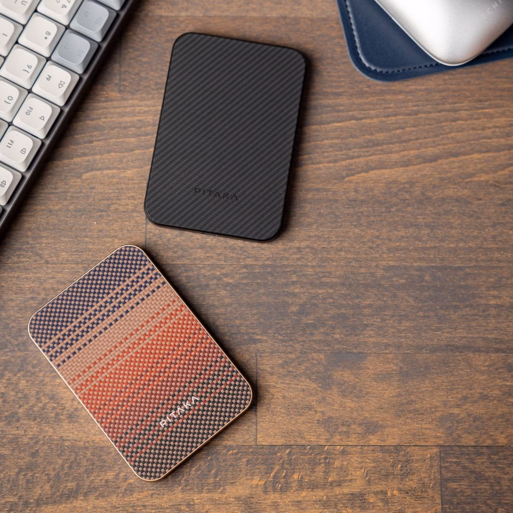 Портативная батарея Pitaka Aramid Fiber Qi2 10000mAh в цветах Sunset и Black из премиального арамидного волокна на деревянном рабочем столе