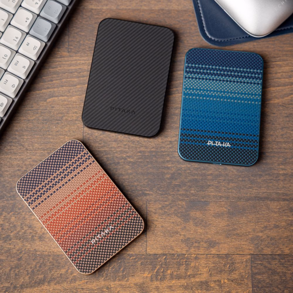 Портативная батарея Pitaka Aramid Fiber Qi2 10000mAh в цветах Sunset и Black из премиального арамидного волокна на деревянном рабочем столе