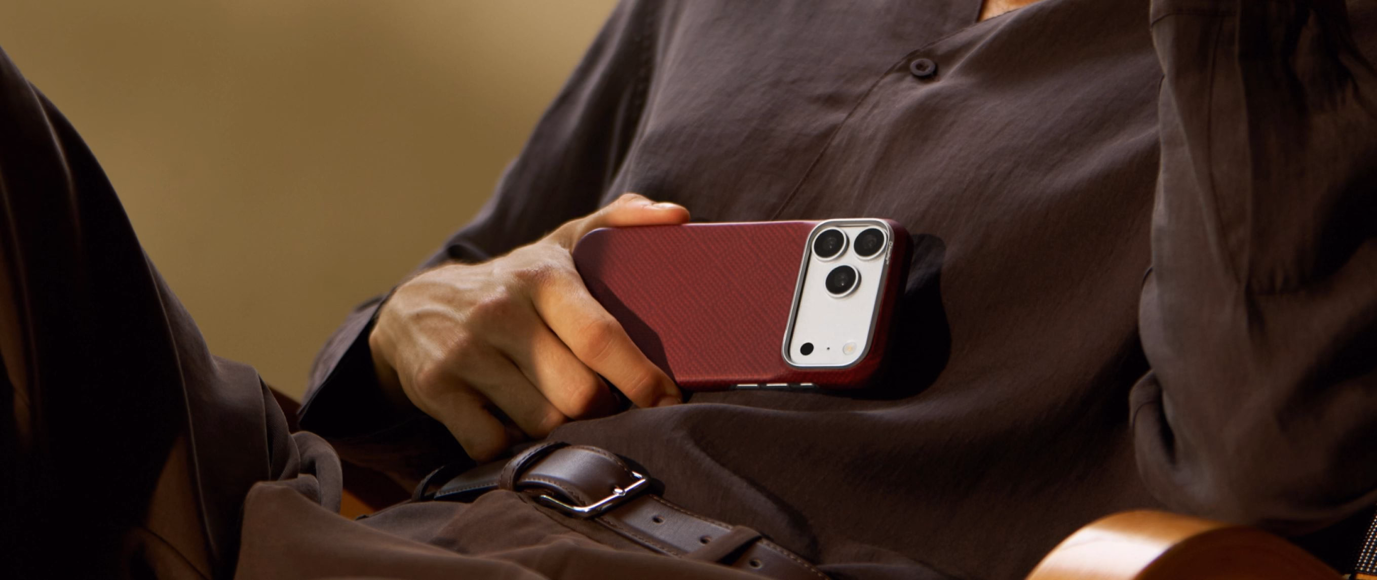 Мужчина держит в руке iPhone 18 Pro Max в чехле Pitaka Edge Ultra-Slim Argyle Burgundy
