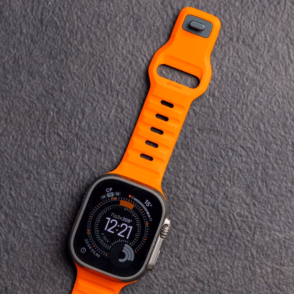 Apple Watch Ultra з встановленим яскраво-помаранчевим ремінцем Nomad Sport Band на темно-сірому фоні, деталізація текстури FKM