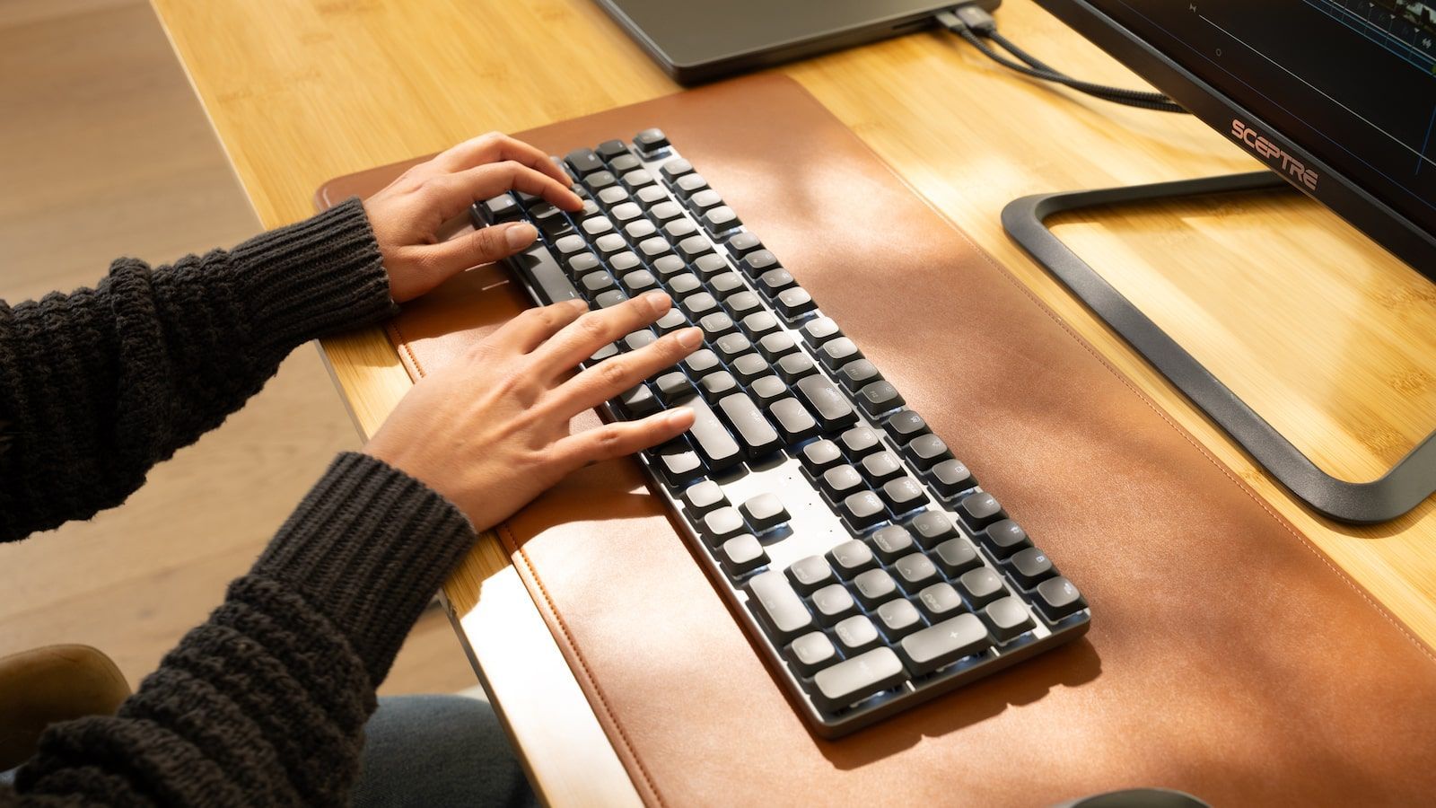 Близький план рук користувача під час роботи на чорній клавіатурі Satechi SM3 Slim, розміщеній на коричневому шкіряному маті.