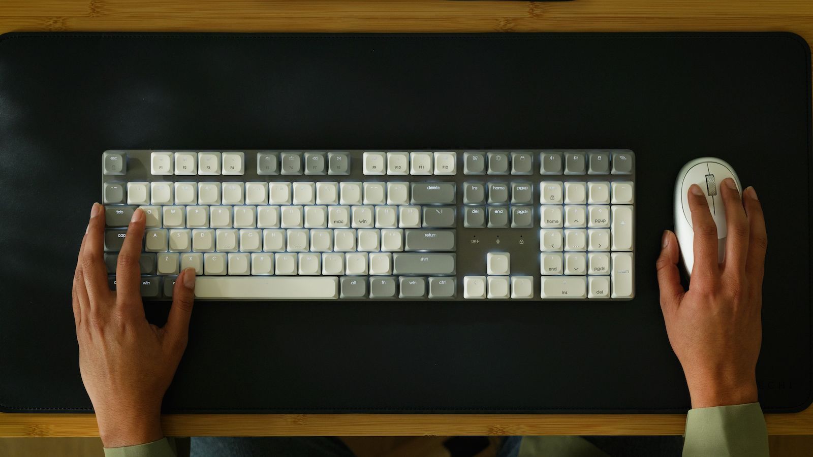 Вигляд зверху на процес друку на світлій клавіатурі Satechi SM3 Slim, що розташована на великому чорному настільному маті.