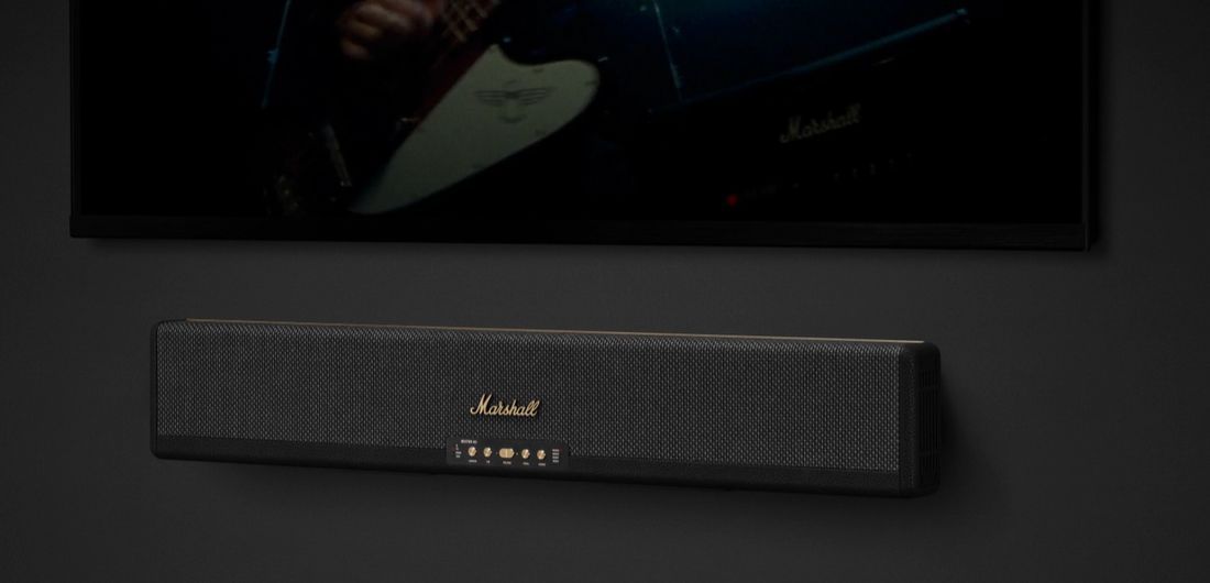 Саундбар Marshall Heston, закріплений на стіні під телевізором, вигляд на фоні темного інтер'єру