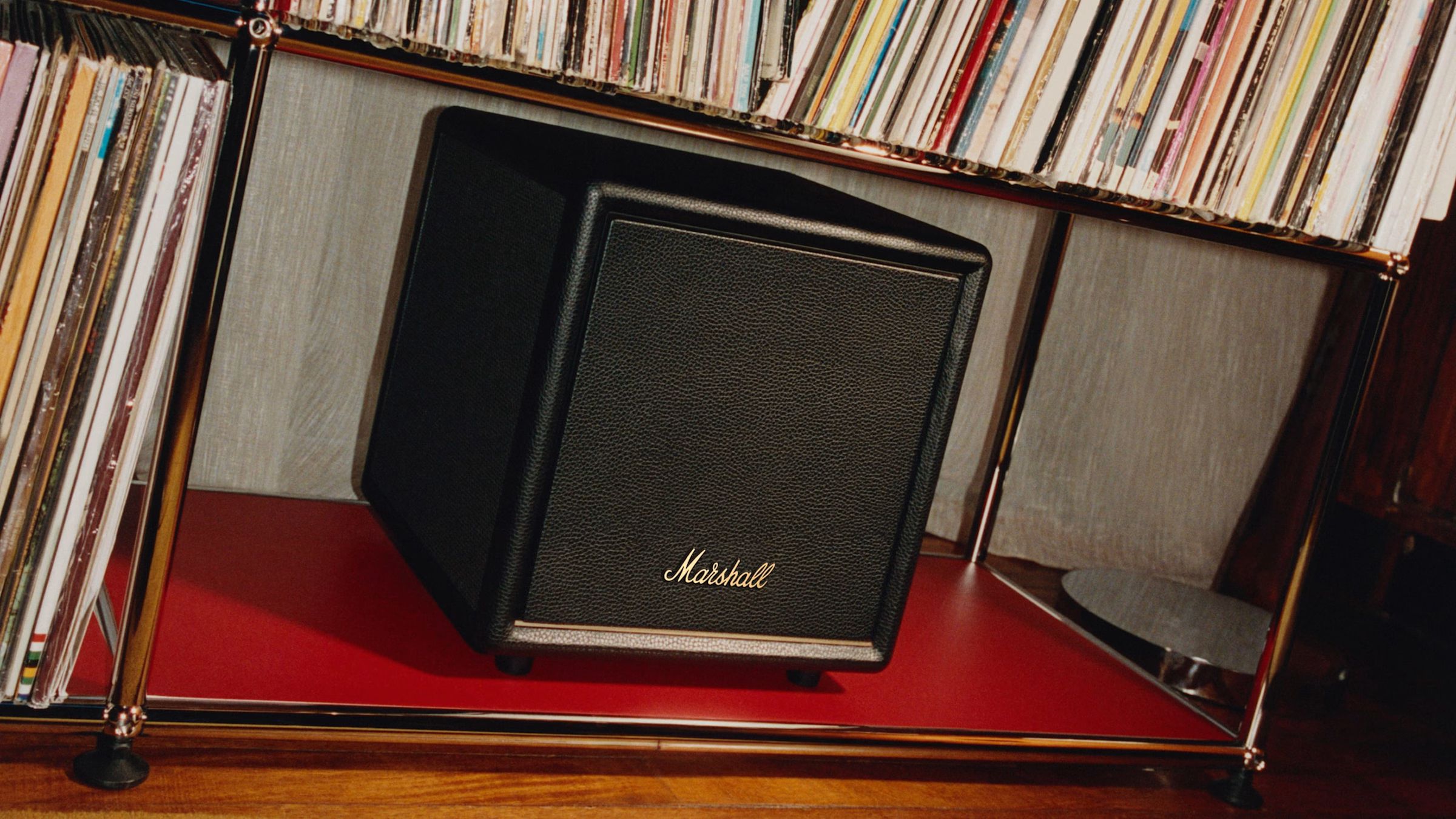 Сабвуфер Marshall Heston у чорному шкіряному корпусі з золотистим логотипом на полиці поруч із вініловими платівками