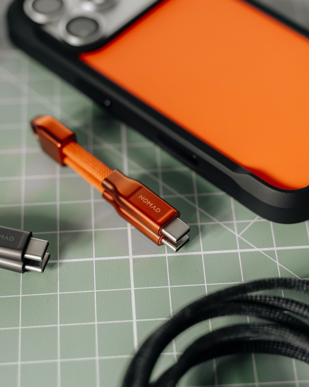 Кабель-брелок Nomad ChargeKey помаранчевого кольору поряд зі смартфоном на робочому столі.